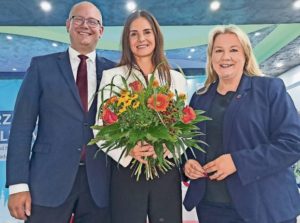 Vanessa-Kim Zobel mit Blumenstrauß in der Hand lächelt gemeinsam mit Marco Moormann und Melanie Reinecke in die Kamera