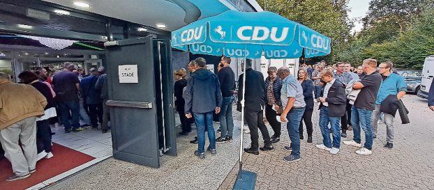 Eine große Anzahl an Personen wartet vor dem Eingang für den Rotenburger Kreisverband, während vor dem Stader Eingang keine Personen warten. In der Mitte steht ein blauer Sonnenschirm mit CDU-Aufschrift.