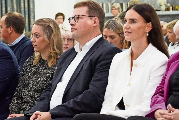 Alexander Krause im Anzug und Vanessa-Kim Zobel im weißen Blazer sitzen nebeneinander in der ersten Reihe.